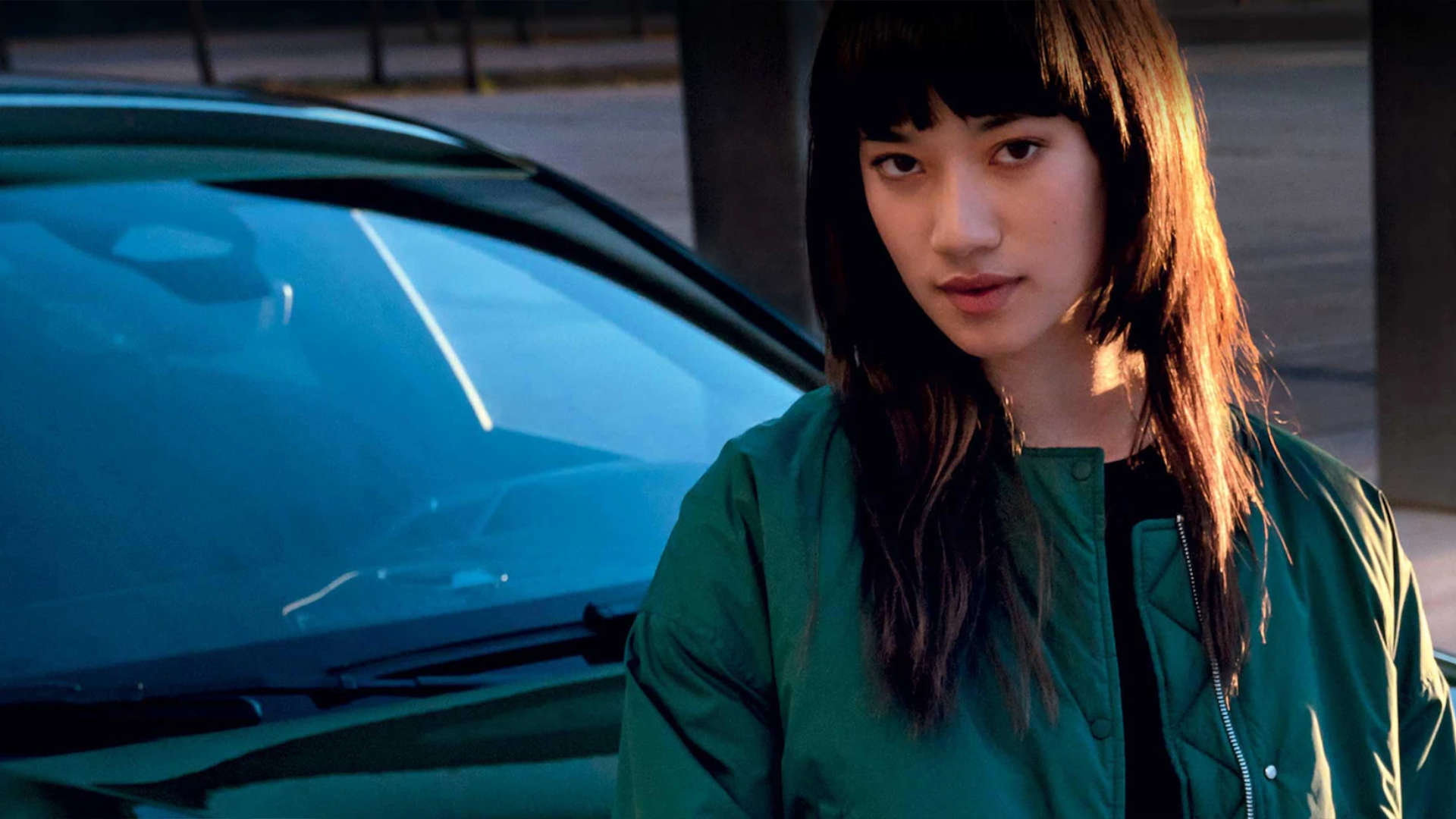 Дівчина в зеленій куртці стоїть перед автомобілем Peugeot